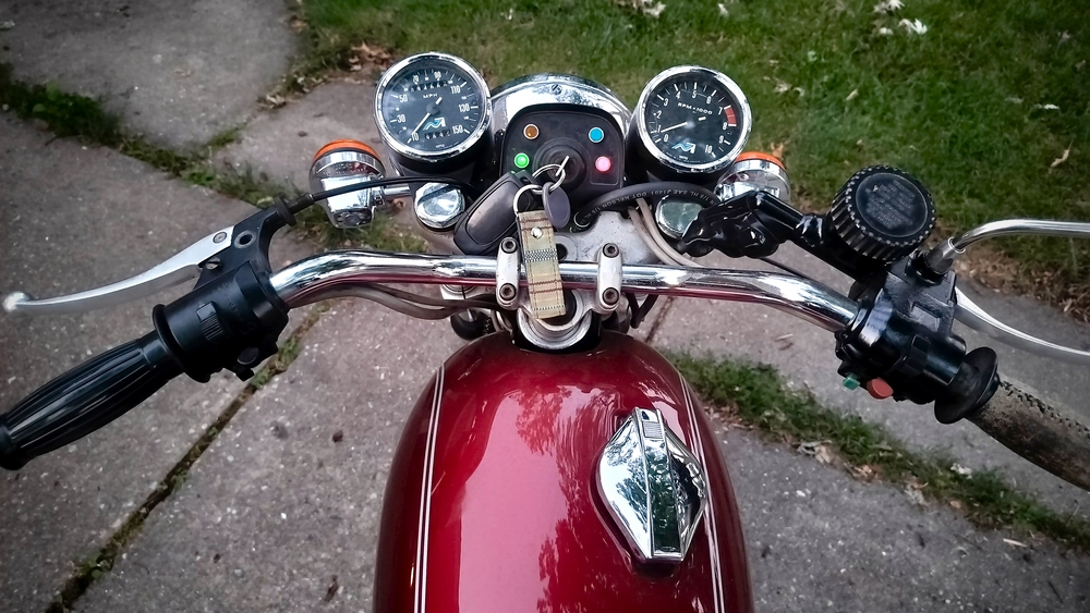 Controls area of the 1975 Norton. Small tachometer and speedometer pods, key area, four unmarked indicator lights, and standard thumb controls.
