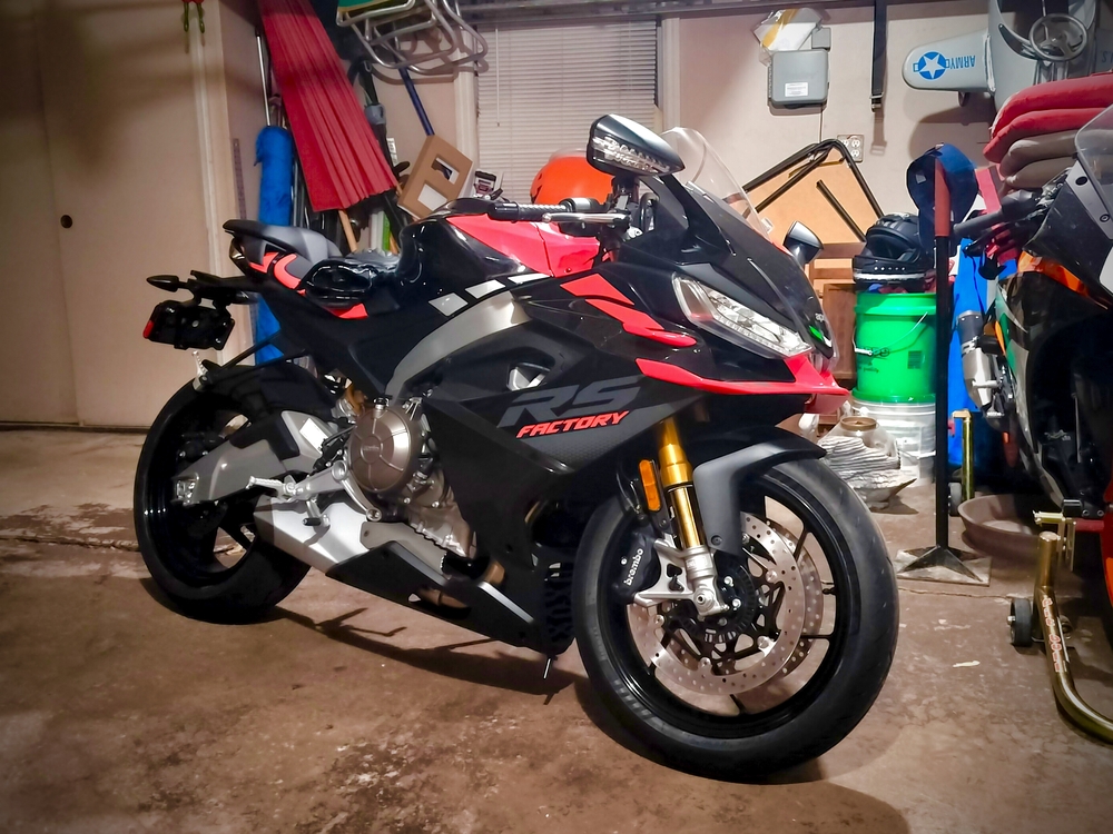 2023 Aprilia RS 660 next to a race-prepped KTM RC 390 in a two-car garage.