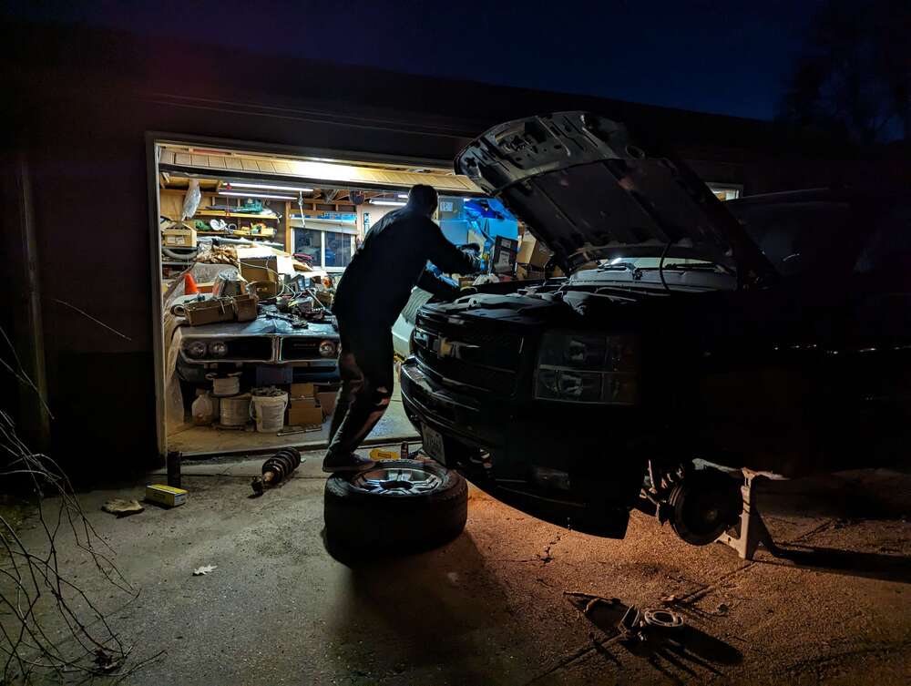 Ben looking at engine bay while standing on tire in front of the truck.